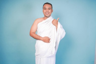 Heyecanlı Asyalı Müslüman adam ihram jesti pozu veriyor, izole edilmiş mavi arka plan. Hac konsepti. İslam Müslüman konsepti