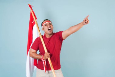 Endonezyalı genç adam elinde bir bayrak tutarken yumruğunu kaldırıyor ve Bağımsızlık Günü konsepti olan Endonezya 'ya bağırıyor..