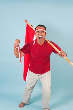 Endonezyalı genç adam elinde bir bayrak tutarken yumruğunu kaldırıyor ve Bağımsızlık Günü konsepti olan Endonezya 'ya bağırıyor..