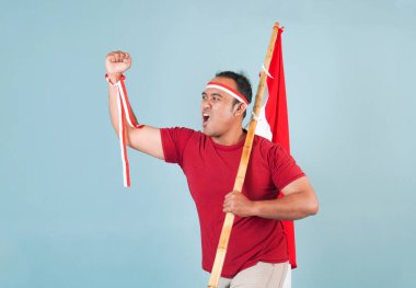 Endonezyalı genç adam elinde bir bayrak tutarken yumruğunu kaldırıyor ve Bağımsızlık Günü konsepti olan Endonezya 'ya bağırıyor..