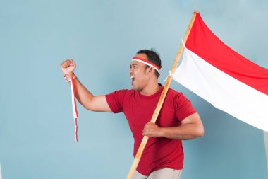 Endonezyalı genç adam elinde bir bayrak tutarken yumruğunu kaldırıyor ve Bağımsızlık Günü konsepti olan Endonezya 'ya bağırıyor..