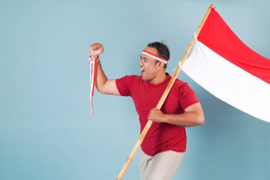 Endonezyalı genç adam elinde bir bayrak tutarken yumruğunu kaldırıyor ve Bağımsızlık Günü konsepti olan Endonezya 'ya bağırıyor..