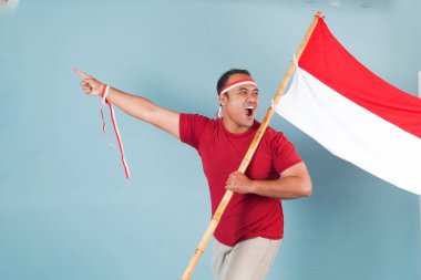 Endonezyalı genç adam elinde bir bayrak tutarken yumruğunu kaldırıyor ve Bağımsızlık Günü konsepti olan Endonezya 'ya bağırıyor..
