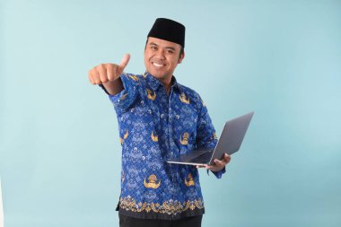 Elinde dizüstü bilgisayarı olan kopri mavi batik üniformalı bir devlet çalışanı gülümsüyor ve ASN devlet memuru konseptini onaylıyor..