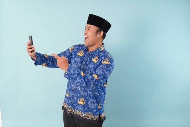 Kopri Blue Batik üniforması giyen gülümseyen devlet çalışanı akıllı telefonunu işaret ederken görüntülü arama yapıyor. PNS, ASN memur konsepti.