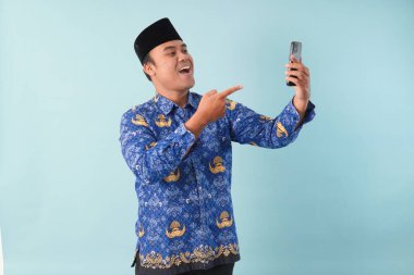 Kopri Blue Batik üniforması giyen gülümseyen devlet çalışanı akıllı telefonunu işaret ederken görüntülü arama yapıyor. PNS, ASN memur konsepti.