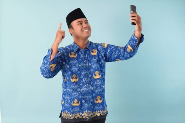 Kopri Blue Batik üniforması giyen gülümseyen devlet çalışanı akıllı telefonunu işaret ederken görüntülü arama yapıyor. PNS, ASN memur konsepti.