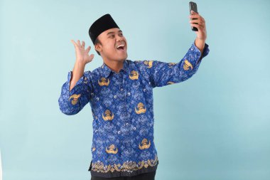 Kopri Blue Batik üniforması giyen gülümseyen devlet çalışanı akıllı telefonunu işaret ederken görüntülü arama yapıyor. PNS, ASN memur konsepti.