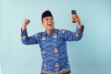 Kopri Blue Batik üniforması giyen gülümseyen devlet çalışanı akıllı telefonunu işaret ederken görüntülü arama yapıyor. PNS, ASN memur konsepti.