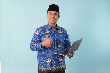 Elinde dizüstü bilgisayarı olan kopri mavi batik üniformalı bir devlet çalışanı gülümsüyor ve ASN devlet memuru konseptini onaylıyor..