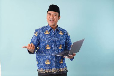 Elinde dizüstü bilgisayarı olan kopri mavi batik üniformalı bir devlet çalışanı gülümsüyor ve ASN devlet memuru konseptini onaylıyor..