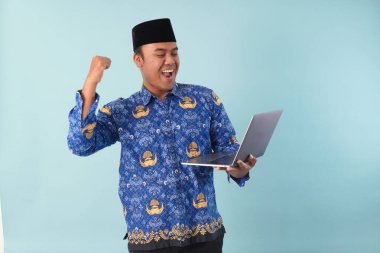 Elinde dizüstü bilgisayarı olan kopri mavi batik üniformalı bir devlet çalışanı gülümsüyor ve ASN devlet memuru konseptini onaylıyor..