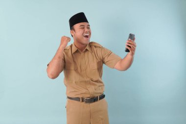 Haki üniformalı gülümseyen devlet memuru akıllı telefonuna, ASN devlet memuru konseptine işaret ederken video çağrısı yapıyor..