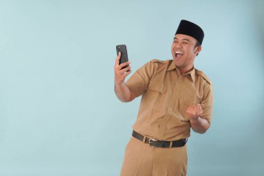 Haki üniformalı gülümseyen devlet memuru akıllı telefonuna, ASN devlet memuru konseptine işaret ederken video çağrısı yapıyor..