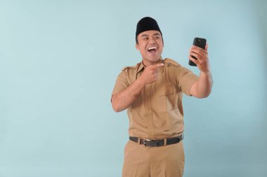 Haki üniformalı gülümseyen devlet memuru akıllı telefonuna, ASN devlet memuru konseptine işaret ederken video çağrısı yapıyor..