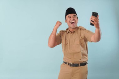 Haki üniformalı gülümseyen devlet memuru akıllı telefonuna, ASN devlet memuru konseptine işaret ederken video çağrısı yapıyor..