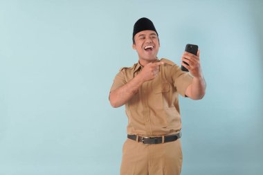 Haki üniformalı gülümseyen devlet memuru akıllı telefonuna, ASN devlet memuru konseptine işaret ederken video çağrısı yapıyor..