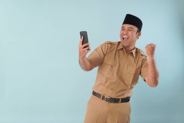 Haki üniformalı gülümseyen devlet memuru akıllı telefonuna, ASN devlet memuru konseptine işaret ederken video çağrısı yapıyor..