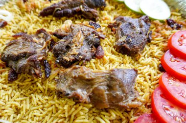 Geleneksel kebuli pilavı, aromatik baharatlı pirinç yemeği, taze et, kuru üzüm, salatalık, soğan, baharat ve taze domates dilimleri ile servis edilir.