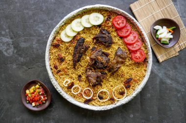 Geleneksel kebuli pilavı, aromatik baharatlı pirinç yemeği, taze et, kuru üzüm, salatalık, soğan, baharat ve taze domates dilimleri ile servis edilir.