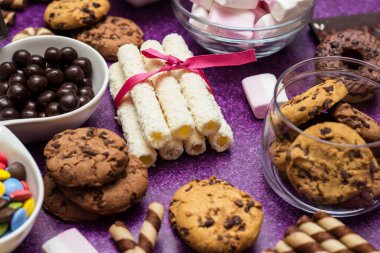 Çikolata ve bisküvi arka planda. Bir sürü çikolata, şeker, kurabiye, bisküvi, kek, çörek ve diğer tatlılar. Sütlü çikolata, koyu çikolata, waffle hindistan cevizi. Mor arkaplan