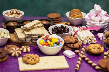 Çikolata ve bisküvi arka planda. Bir sürü çikolata, şeker, kurabiye, bisküvi, kek, çörek ve diğer tatlılar. Sütlü çikolata, koyu çikolata, waffle hindistan cevizi. Mor arkaplan