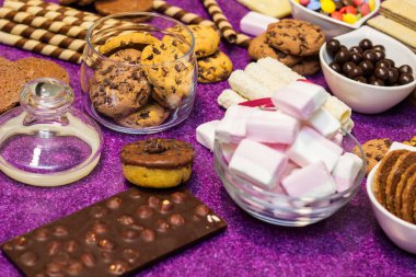 Çikolata ve bisküvi arka planda. Bir sürü çikolata, şeker, kurabiye, bisküvi, kek, çörek ve diğer tatlılar. Sütlü çikolata, koyu çikolata, waffle hindistan cevizi. Mor arkaplan