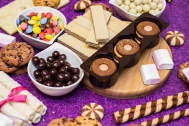 Çikolata ve bisküvi arka planda. Bir sürü çikolata, şeker, kurabiye, bisküvi, kek, çörek ve diğer tatlılar. Sütlü çikolata, koyu çikolata, waffle hindistan cevizi. Mor arkaplan