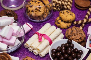 Çikolata ve bisküvi arka planda. Bir sürü çikolata, şeker, kurabiye, bisküvi, kek, çörek ve diğer tatlılar. Sütlü çikolata, koyu çikolata, waffle hindistan cevizi. Mor arkaplan