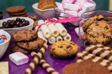 Çikolata ve bisküvi arka planda. Bir sürü çikolata, şeker, kurabiye, bisküvi, kek, çörek ve diğer tatlılar. Sütlü çikolata, koyu çikolata, waffle hindistan cevizi. Mor arkaplan