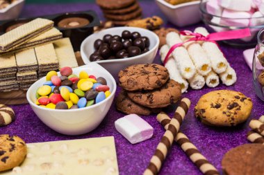 Çikolata ve bisküvi arka planda. Bir sürü çikolata, şeker, kurabiye, bisküvi, kek, çörek ve diğer tatlılar. Sütlü çikolata, koyu çikolata, waffle hindistan cevizi. Mor arkaplan