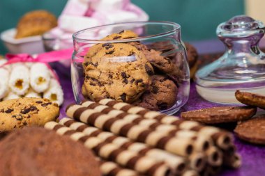 Çikolata ve bisküvi arka planda. Bir sürü çikolata, şeker, kurabiye, bisküvi, kek, çörek ve diğer tatlılar. Sütlü çikolata, koyu çikolata, waffle hindistan cevizi. Mor arkaplan
