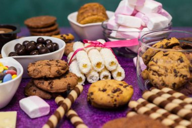 Çikolata ve bisküvi arka planda. Bir sürü çikolata, şeker, kurabiye, bisküvi, kek, çörek ve diğer tatlılar. Sütlü çikolata, koyu çikolata, waffle hindistan cevizi. Mor arkaplan