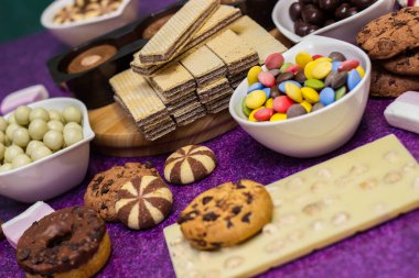 Çikolata ve bisküvi arka planda. Bir sürü çikolata, şeker, kurabiye, bisküvi, kek, çörek ve diğer tatlılar. Sütlü çikolata, koyu çikolata, waffle hindistan cevizi. Mor arkaplan