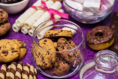 Çikolata ve bisküvi arka planda. Bir sürü çikolata, şeker, kurabiye, bisküvi, kek, çörek ve diğer tatlılar. Sütlü çikolata, koyu çikolata, waffle hindistan cevizi. Mor arkaplan