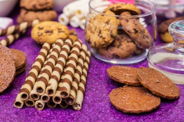 Çikolata ve bisküvi arka planda. Bir sürü çikolata, şeker, kurabiye, bisküvi, kek, çörek ve diğer tatlılar. Sütlü çikolata, koyu çikolata, waffle hindistan cevizi. Mor arkaplan