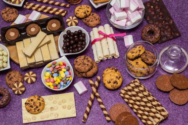 Çikolata ve bisküvi arka planda. Bir sürü çikolata, şeker, kurabiye, bisküvi, kek, çörek ve diğer tatlılar. Sütlü çikolata, koyu çikolata, waffle hindistan cevizi. Mor arkaplan