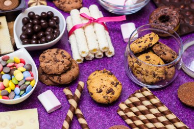 Çikolata ve bisküvi arka planda. Bir sürü çikolata, şeker, kurabiye, bisküvi, kek, çörek ve diğer tatlılar. Sütlü çikolata, koyu çikolata, waffle hindistan cevizi. Mor arkaplan