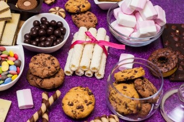 Çikolata ve bisküvi arka planda. Bir sürü çikolata, şeker, kurabiye, bisküvi, kek, çörek ve diğer tatlılar. Sütlü çikolata, koyu çikolata, waffle hindistan cevizi. Mor arkaplan