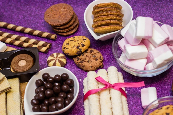 Chocolate and biscuits background. Many pieces of chocolate, candies, cookies, biscuits, cakes, donuts, and other sweets. Milk chocolate and dark chocolate, waffle coconut. Purple background