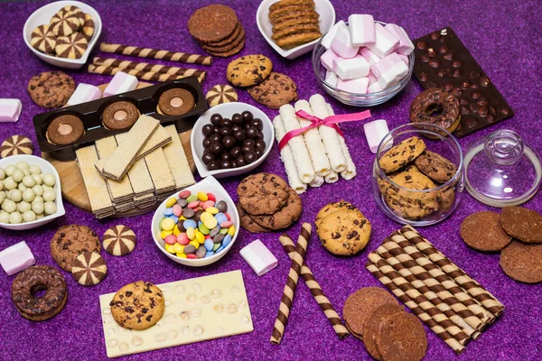 Chocolate and biscuits background. Many pieces of chocolate, candies, cookies, biscuits, cakes, donuts, and other sweets. Milk chocolate and dark chocolate, waffle coconut. Purple background