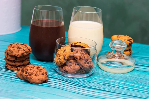 Chocolate chip cookies in a jar with glasses of milk on the blue background