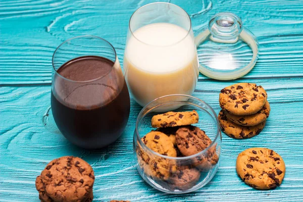 Chocolate chip cookies in a jar with glasses of milk on the blue background