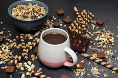 Çikolatalı tahıl gevreği, çikolatalı süt ve waffle rulosu, siyah arka planda mavi bir kasede.