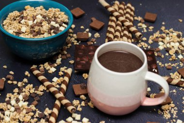 Çikolatalı tahıl gevreği, çikolatalı süt ve waffle rulosu, siyah arka planda mavi bir kasede.