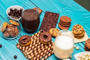 Kavanozda çikolata parçacıklı kurabiyeler ve mavi arka planda bir bardak sütle bir yığın tatlı.