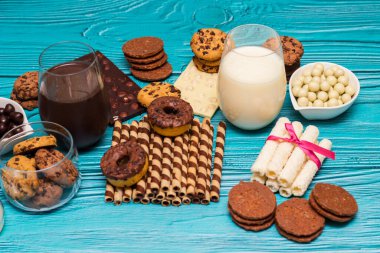 Kavanozda çikolata parçacıklı kurabiyeler ve mavi arka planda bir bardak sütle bir yığın tatlı.