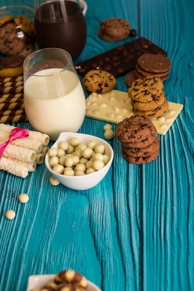 Chocolate chip cookies in a jar and heap of sweets with glasses of milk on the blue background