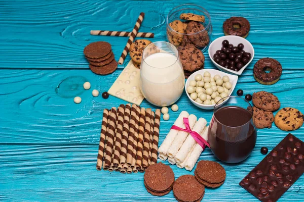 Chocolate chip cookies in a jar and heap of sweets with glasses of milk on the blue background