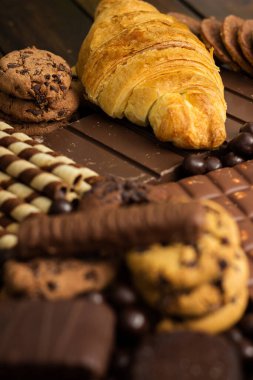 Çikolata dolgulu taze kruvasan ve kırsal arka planda çeşitli çikolatalar ve kurabiyeler.
